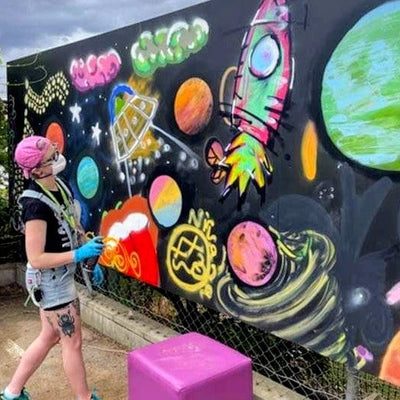 Person standing in front of a colorful mural with bright, glowing elements.
